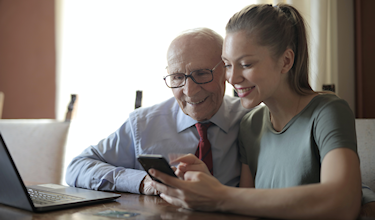 Afbeelding oudere man en jonge vrouw kijken op apparaten